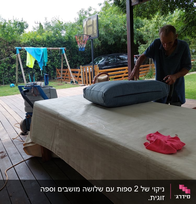 אדם מנקה כרית ספה עם שואב אבק בחצר